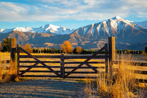 A farm gate with rural land and mountains in the background