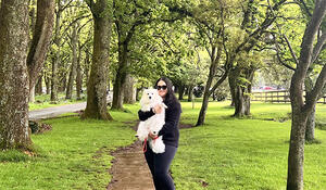 GIS graduate Shalini Mukherjee holding a white dog surrounded by green trees